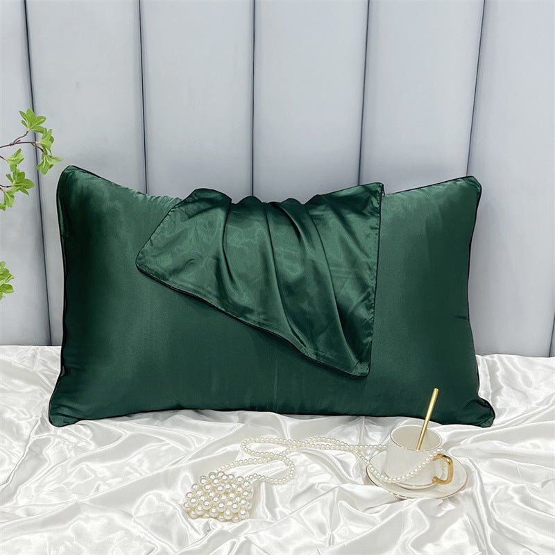 An Aloha Relax Cooling Beauty Sleep Pillowcase, featuring double-sided ice silk for hair and skin protection, adorns a quilted background with a matching satin scarf. A white teacup, gold spoon, and pearl necklace rest on a glossy surface. To the left, a small plant completes the scene.