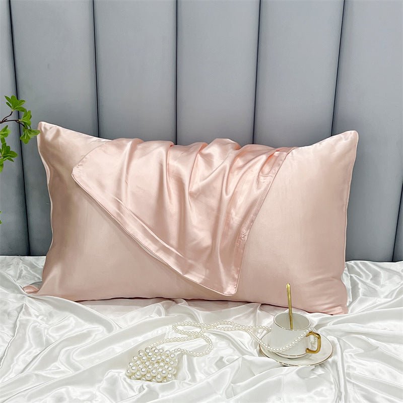 An Aloha Relax Cooling Beauty Sleep Pillowcase made of double-sided ice silk whispers elegance on a white satin bed. Nearby, a cup with a gold spoon sits on its saucer while pearls drape gracefully beside a small plant, all set against vertical gray panels enhancing the serene ambiance.