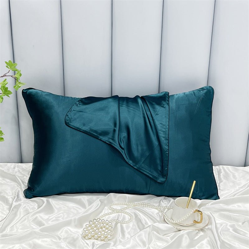 A teal satin Cooling Beauty Sleep Pillowcase by Aloha Relax, paired with a matching eye mask featuring reactive printing, lies on a silky white surface. Nearby are a pearl necklace and white mug with gold handle and spoon. To the left is a small green plant against a light gray background.