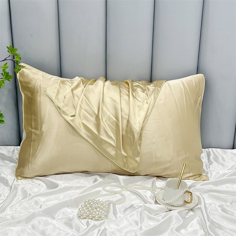 A beige Cooling Beauty Sleep Pillowcase by Aloha Relax, crafted with double-sided ice silk for hair and skin protection using reactive printing, is folded on matching sheets. Nearby, a cup and saucer holds a gold spoon. Pearls and green leaves add elegance against a padded headboard.