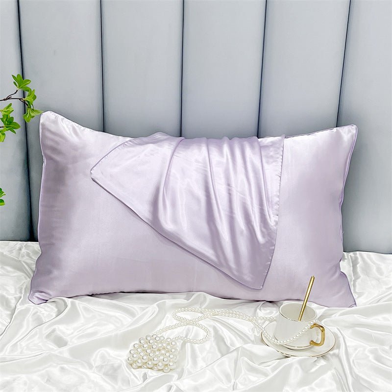 A Cooling Beauty Sleep pillowcase by Aloha Relax in lavender is set on a white silk bedspread, accompanied by a matching scrunchie and pearl necklace. Featuring reactive printing for vibrant hues, the elegant scene includes a white teacup with a gold handle and spoon.