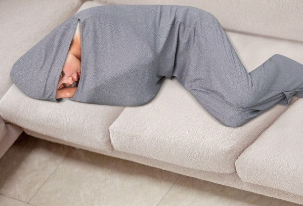 A person is lying on a couch wrapped in an Aloha Relax Comfortable Sleep Pod (for Parent or Child), which snugly covers their entire body and head, with only part of their face visible. The person is lying on their side in a fetal position, experiencing deep stress relief.