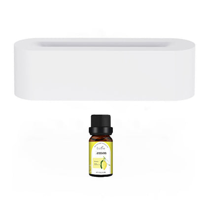 A small bottle of lemon essential oil with a black cap is placed next to the Aloha Relax Flame Aroma Diffuser Air Humidifier. The diffuser, which is white and rectangular, features a sleek, minimalistic design crafted from smooth, solid material perfect for ultrasonic humidification. The bottle's label displays a vibrant lemon graphic.