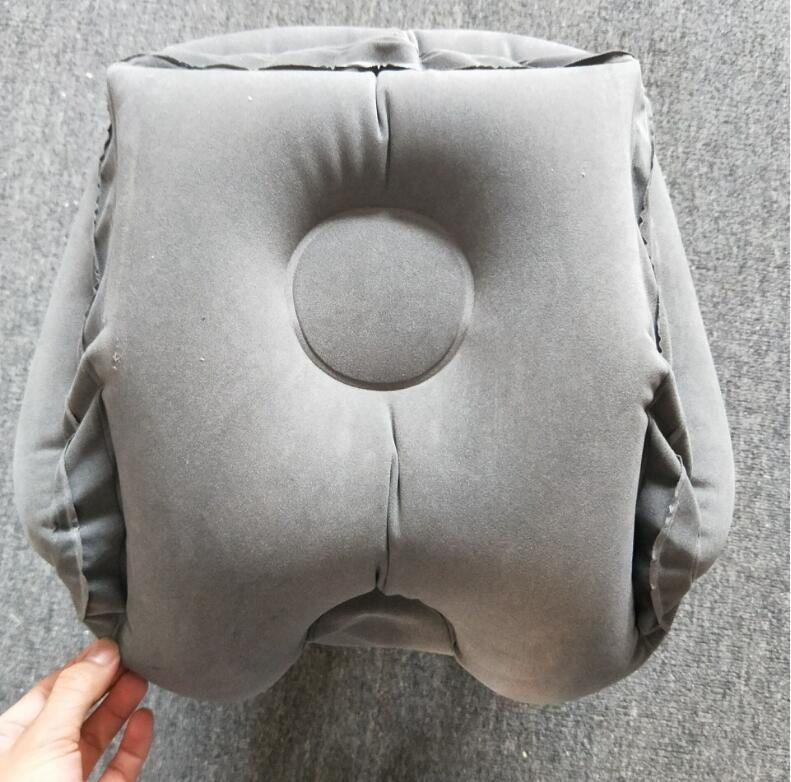 A hand holding the Aloha Relax Inflatable Cushion Travel Pillow, with its gray color, central circular indentation, and recessed sides—ideal for stress relief and sleep improvement—rests on a gray fabric surface.