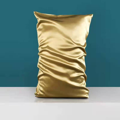 A gold satin pillowcase from Aloha Relax, known as the Double-sided Silk Silk Heavy Sleep Pillowcase, is showcased against a teal wall on a gray surface, evoking palace luxury. The silk fabric shimmers in the light, creating highlights and shadows reminiscent of opulent silk bedding.