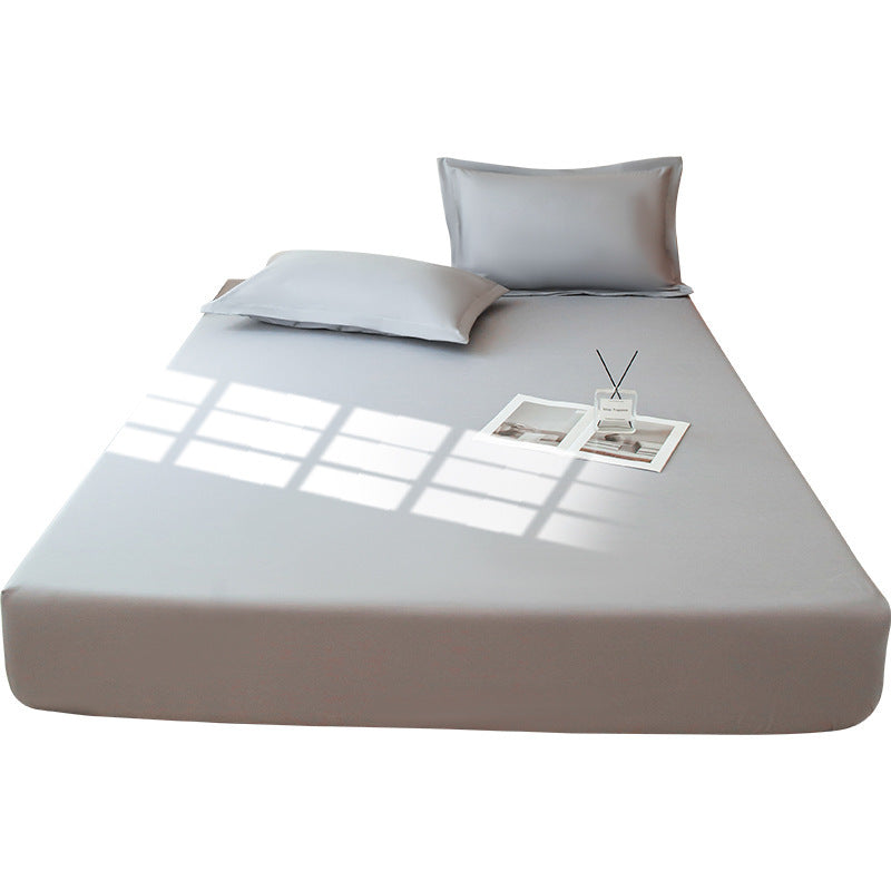 A neatly arranged bed showcases the Aloha Relax Waterproof Mattress Protector in a solid light gray color, complete with two pillows. Sunlight forms window-shaped shadows on the fitted mattress protector. Elegantly placed atop the bed are a small diffuser and an open magazine.