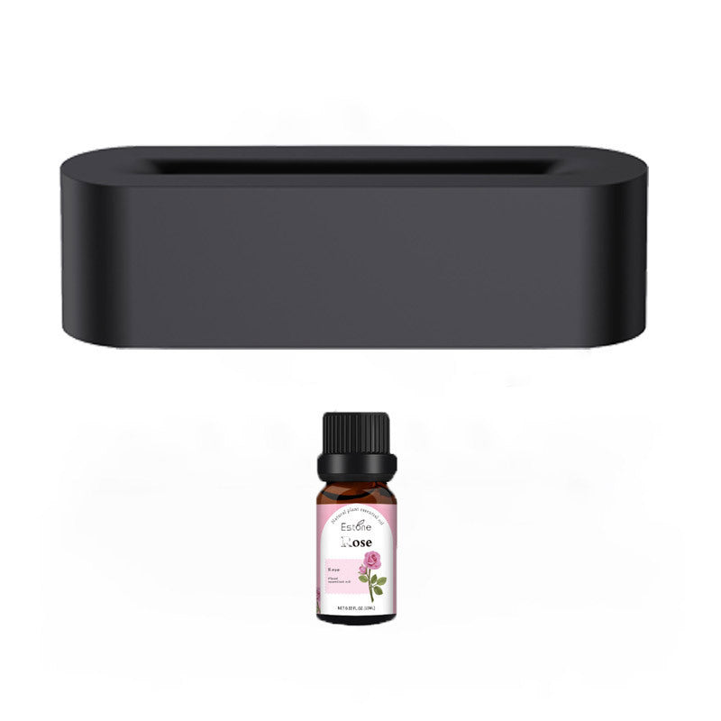 The Flame Aroma Diffuser Air Humidifier from Aloha Relax, a black rectangular device, is situated above a small essential oil bottle featuring a pink label. The bottle displays the scent "rose" against a white background.