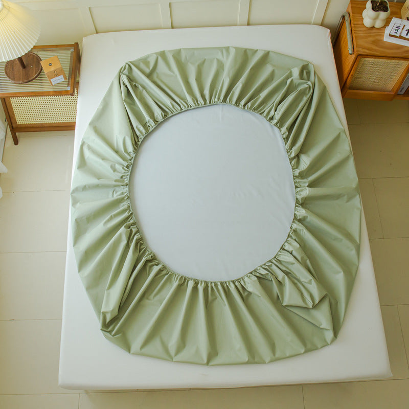 In the bedroom, a Waterproof Mattress Protector Urine Separation Fully Surrounded by Aloha Relax is partially placed on a mattress, highlighting its elastic edges. The room features a wooden nightstand with books and a round lamp, alongside a small wooden table with a box on it. The solid color floor tiles enhance the peaceful atmosphere.